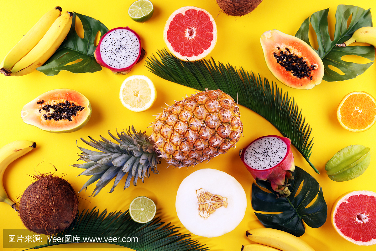 色彩柔和的黄色背景是异国情调的水果和热带棕榈叶-木瓜,芒果,菠萝,香蕉,杨桃,火龙果